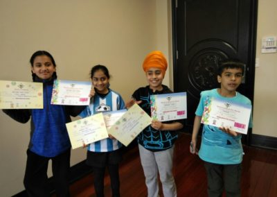 Four children proudly holding their certificates indoors.